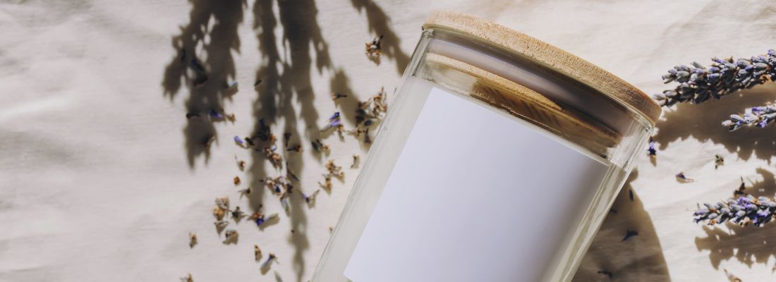 Bougie coulée dans un contenant en verre posée sur un drap entourée de brins de lavande